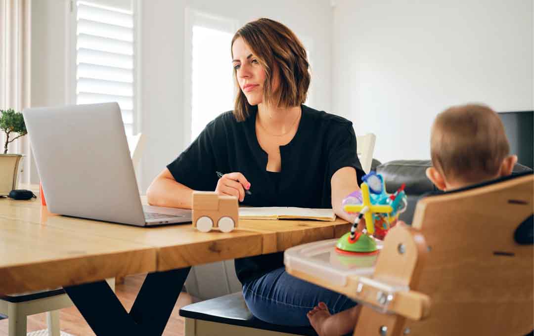 An employee working on a computer while their infant is watching in the foreground.